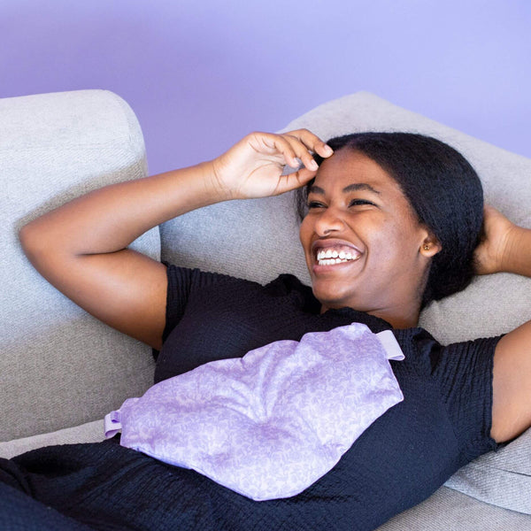 Load image into Gallery viewer, Woman lying on a couch with a purple heating pad on her stomach
